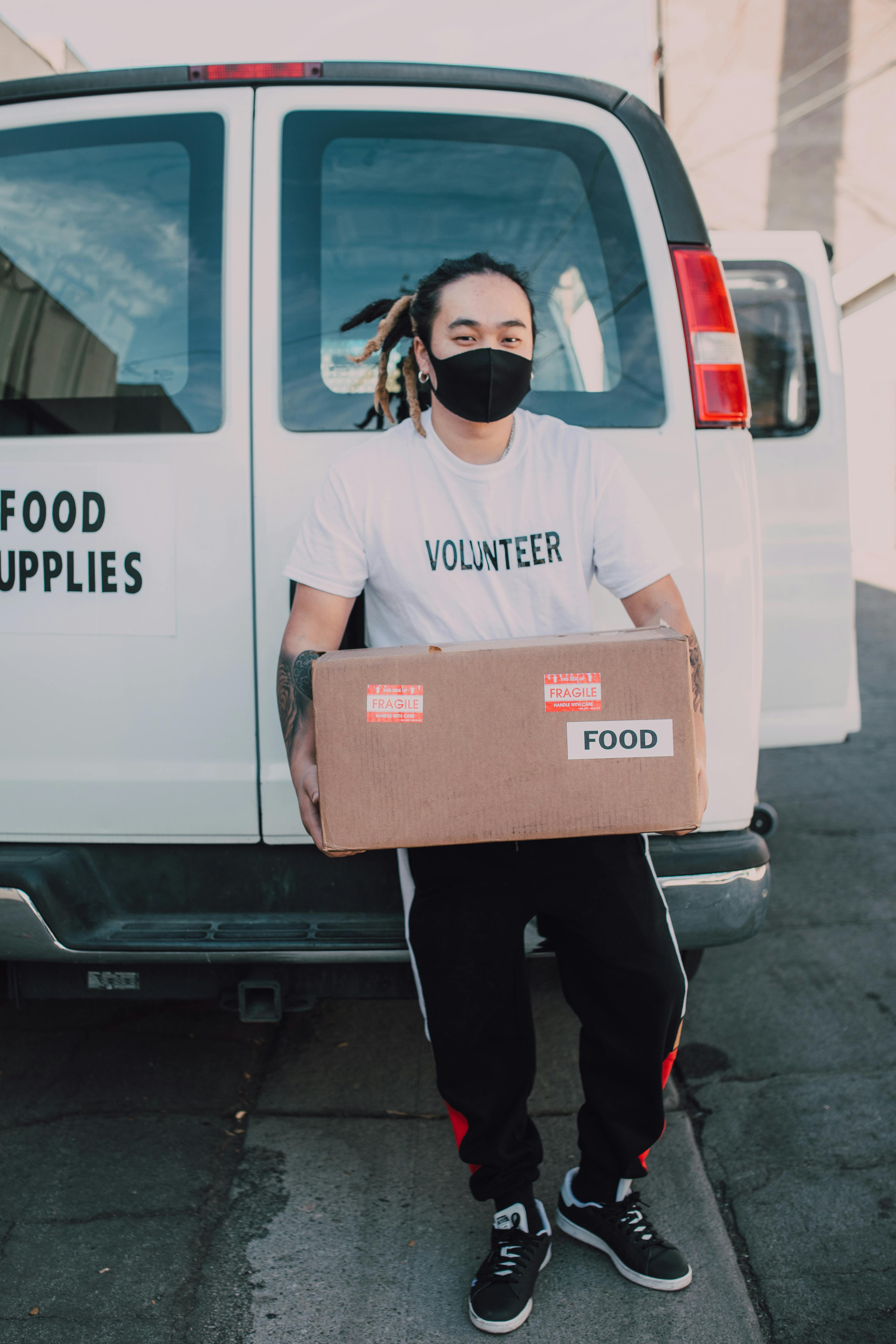 a volunteer wearing face mask holding a carton box with food label