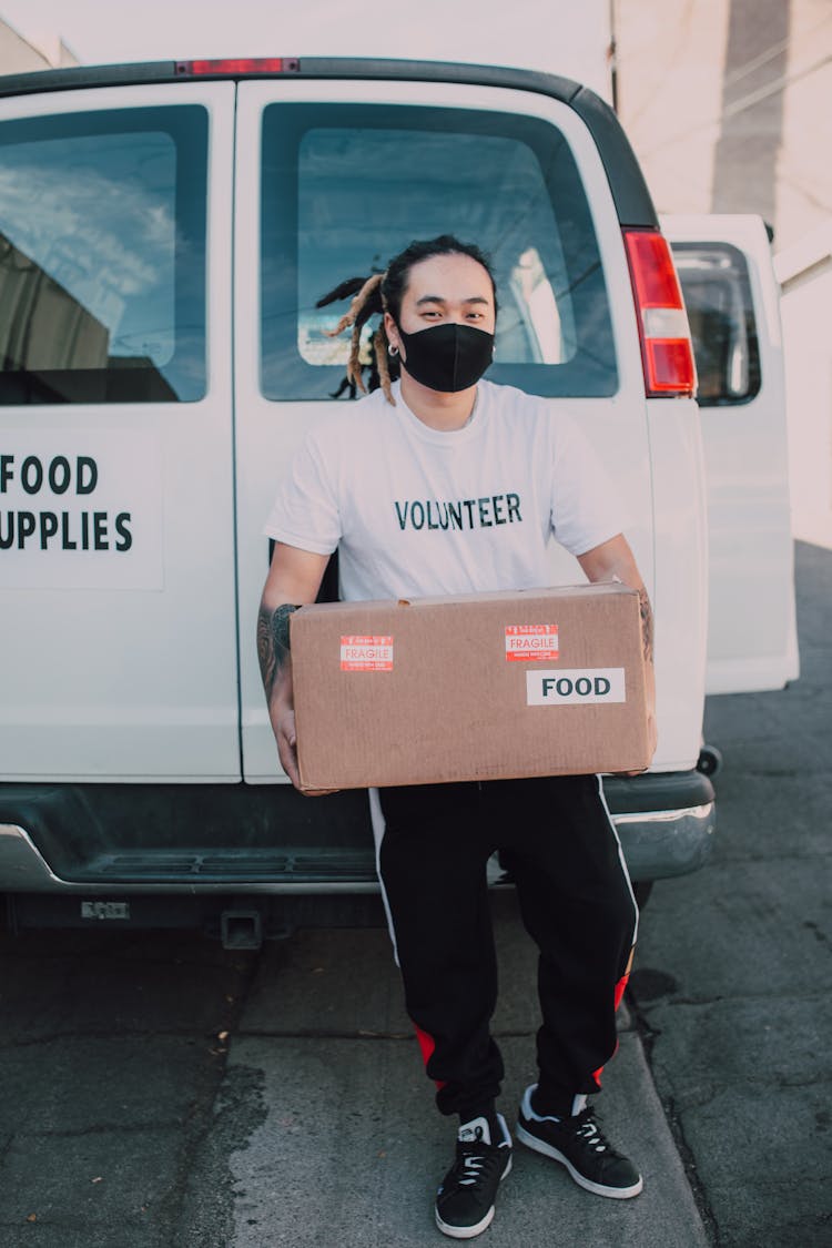 A Volunteer Wearing Face Mask Holding A Carton Box With Food Label
