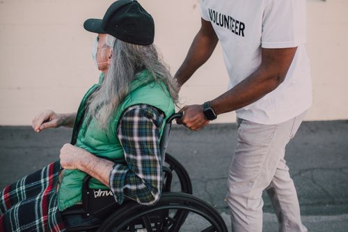 Free A volunteer helps a senior in a wheelchair during daytime outdoors. Stock Photo