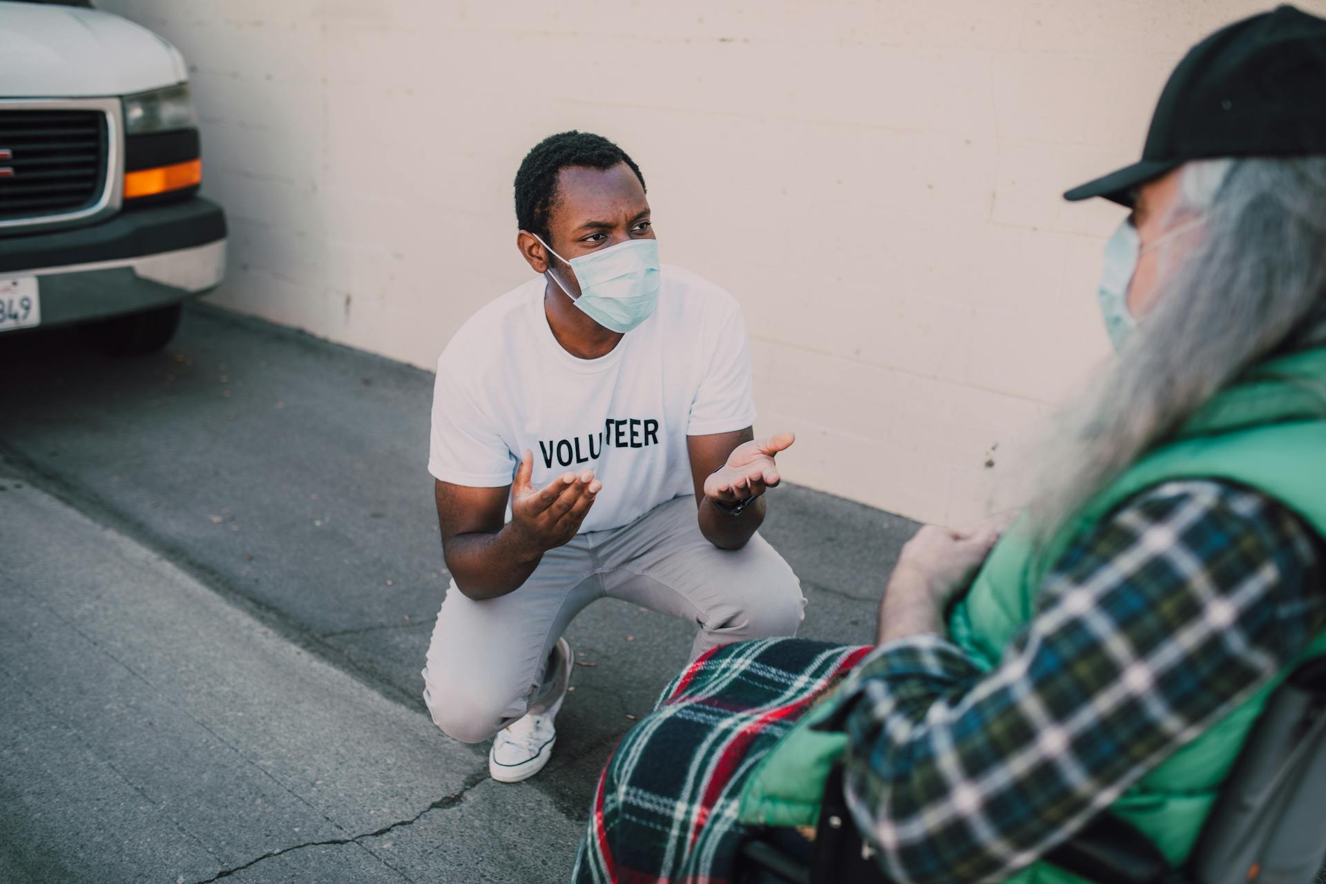 A compassionate volunteer wearing a face mask interacts with a community member outdoors, symbolizing social good.