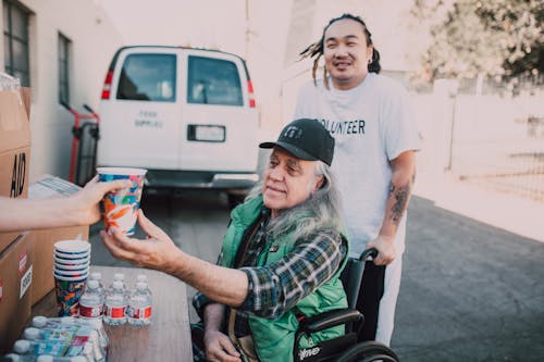 Volunteers Giving Drink to a Wheelchair Bound Elderly