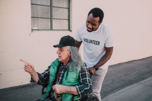 Free A volunteer helps an elderly man in a wheelchair outside, showing community support and care. Stock Photo
