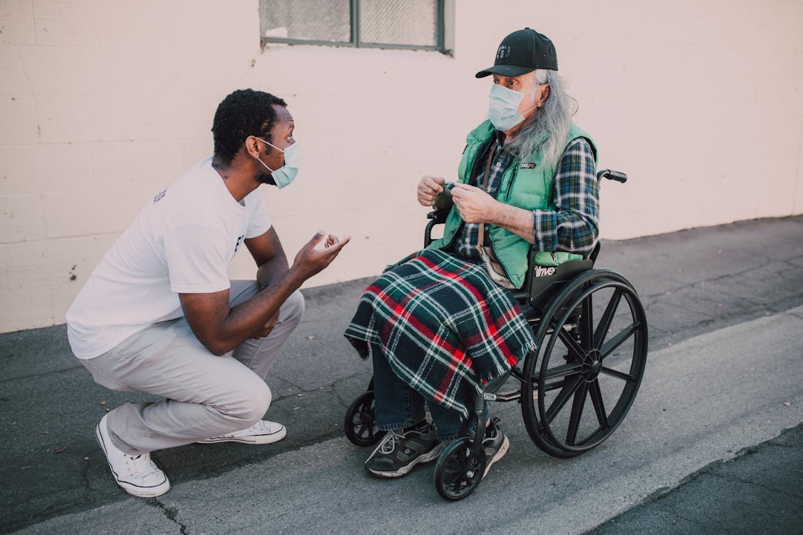 Free A Man Talking to an Elderly Man Sitting on a Wheelchair Stock Photo
