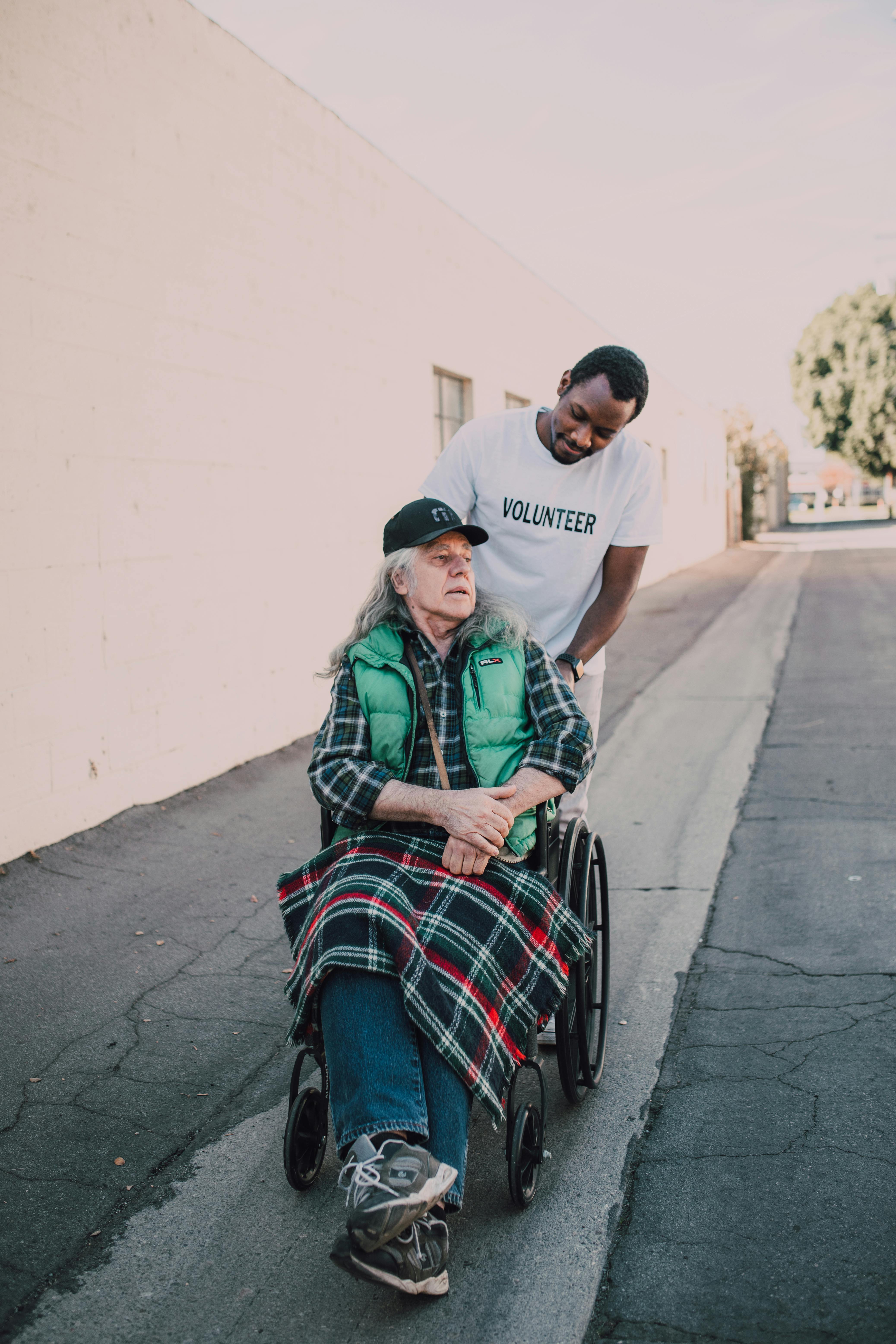 a volunteer pushing an elderly sitting on a wheelchair