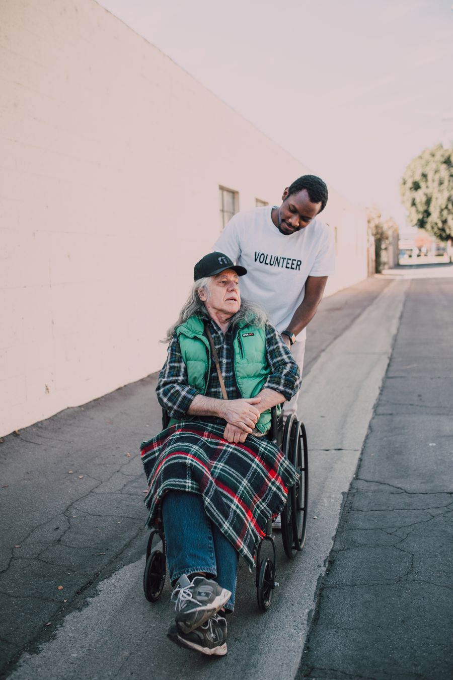 A Filipino volunteer assisting an elderly man in a wheelchair along an outdoor path