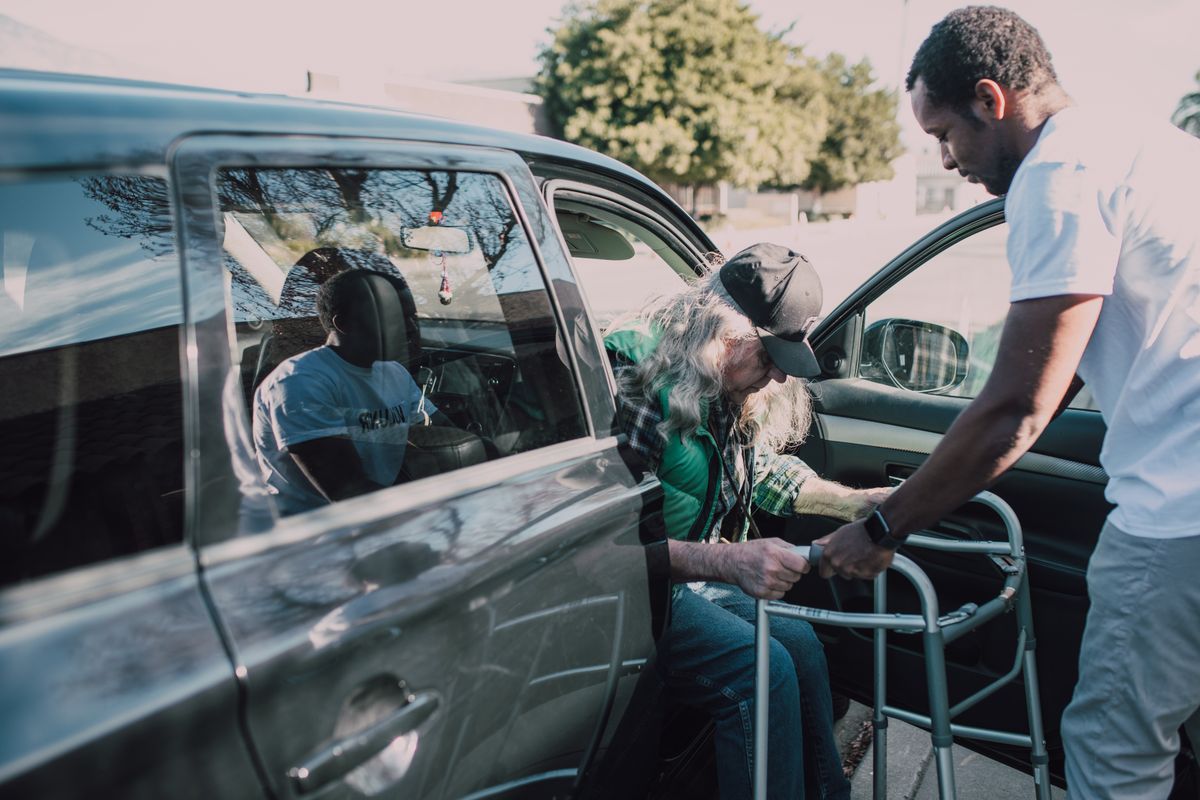A driver helping an older man with his walker into the car on arrival