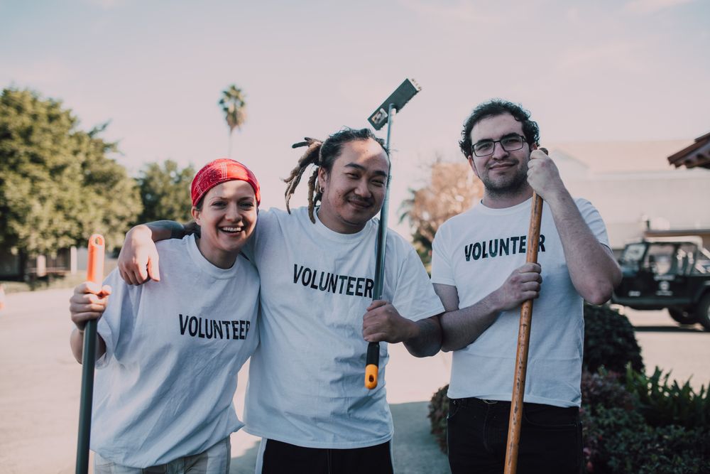 Three volunteers holding cleaning tools during a neighborhood service day