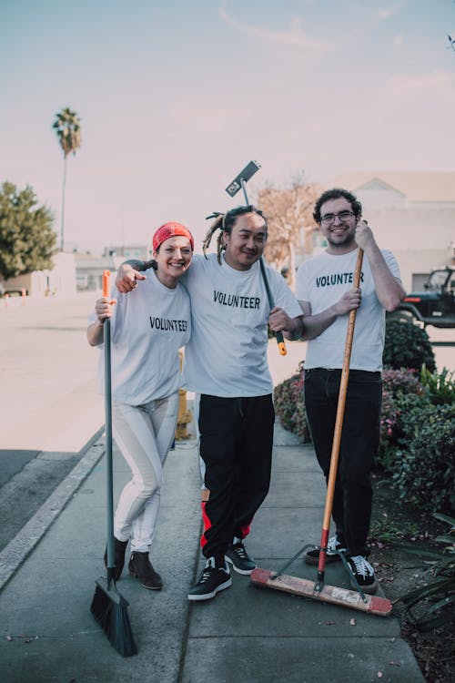 Men and a Woman Standing on the Street while Holding Mops and a Broom