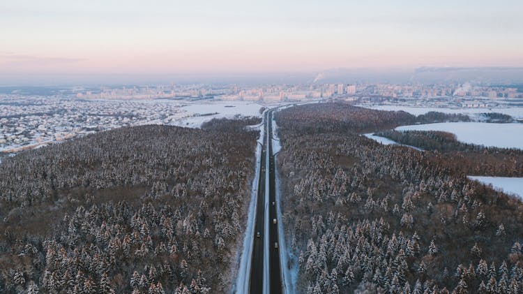 Aerial Shot Of A Highway In A Forest And A City In The Winter