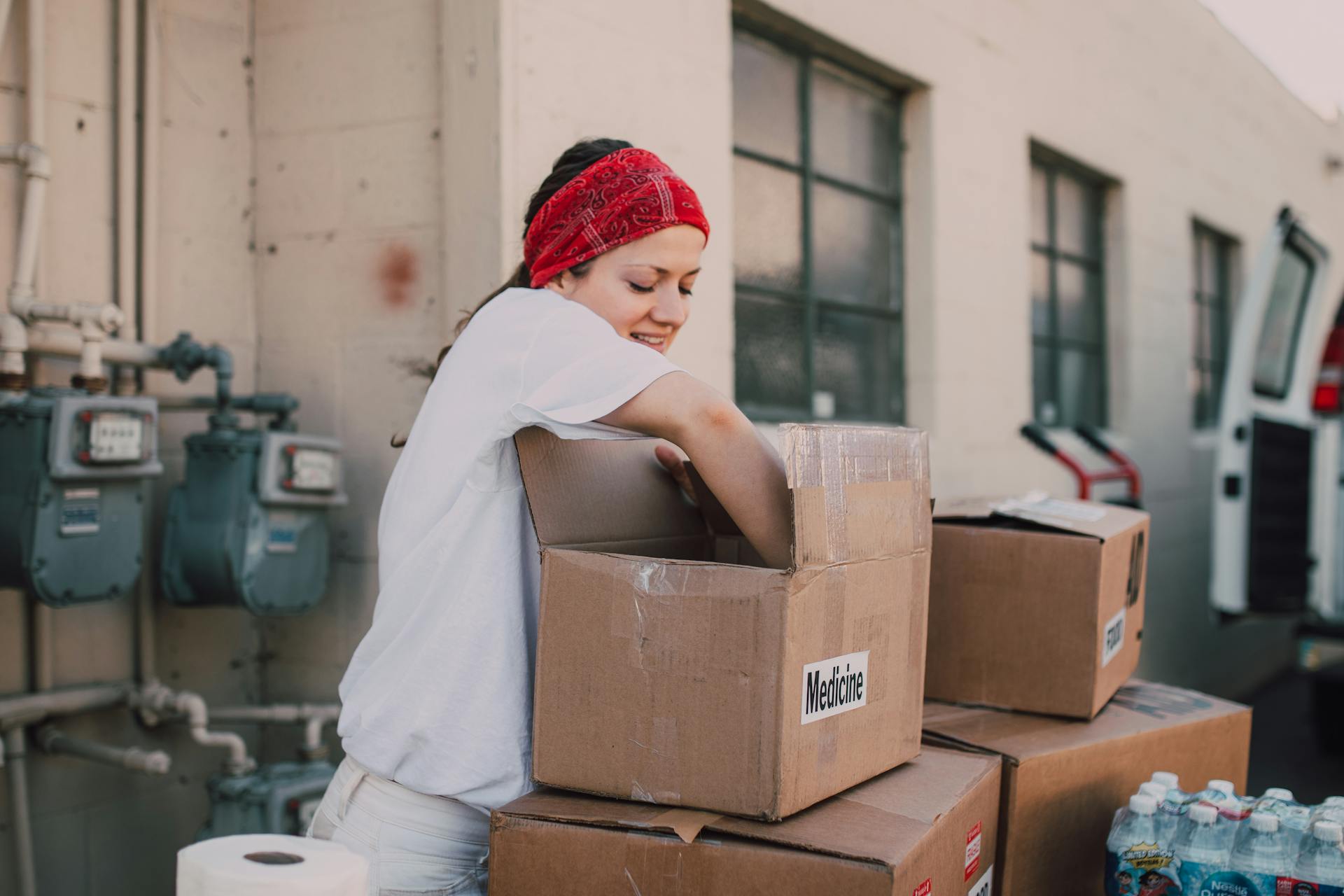 A Woman in White Shirt Standing Beside Boxes of Donations