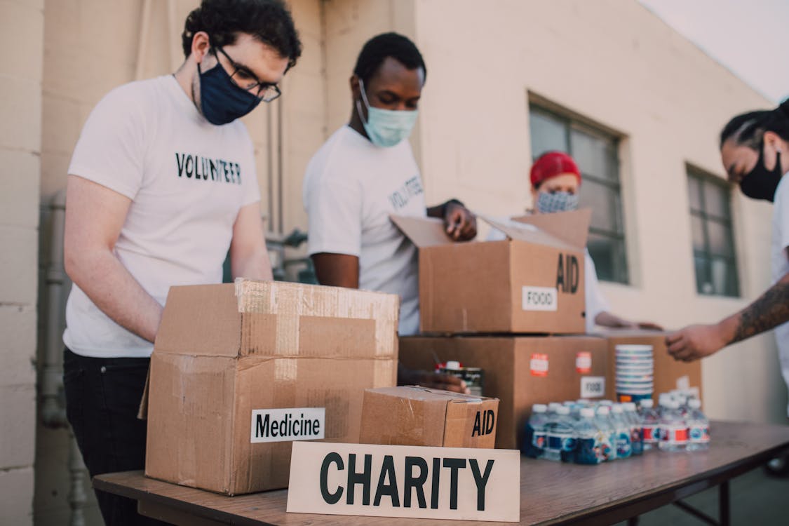 Free Group of volunteers wearing masks organizing donation boxes labeled food and medicine outdoors. Stock Photo