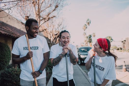 Three diverse volunteers smiling while cleaning the street on a sunny day.