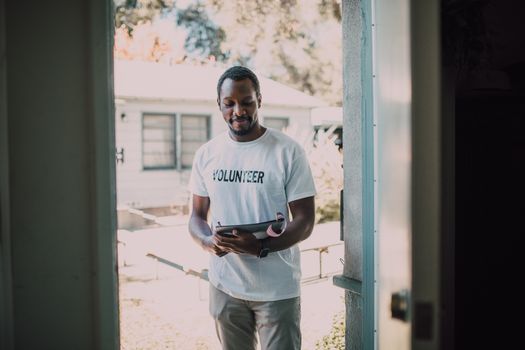 A man wearing a volunteer t-shirt stands by a doorway holding a tablet, engaged in a community event.