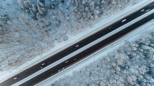 Aerial shot of a winter highway cutting through a snowy forest in Belarus.