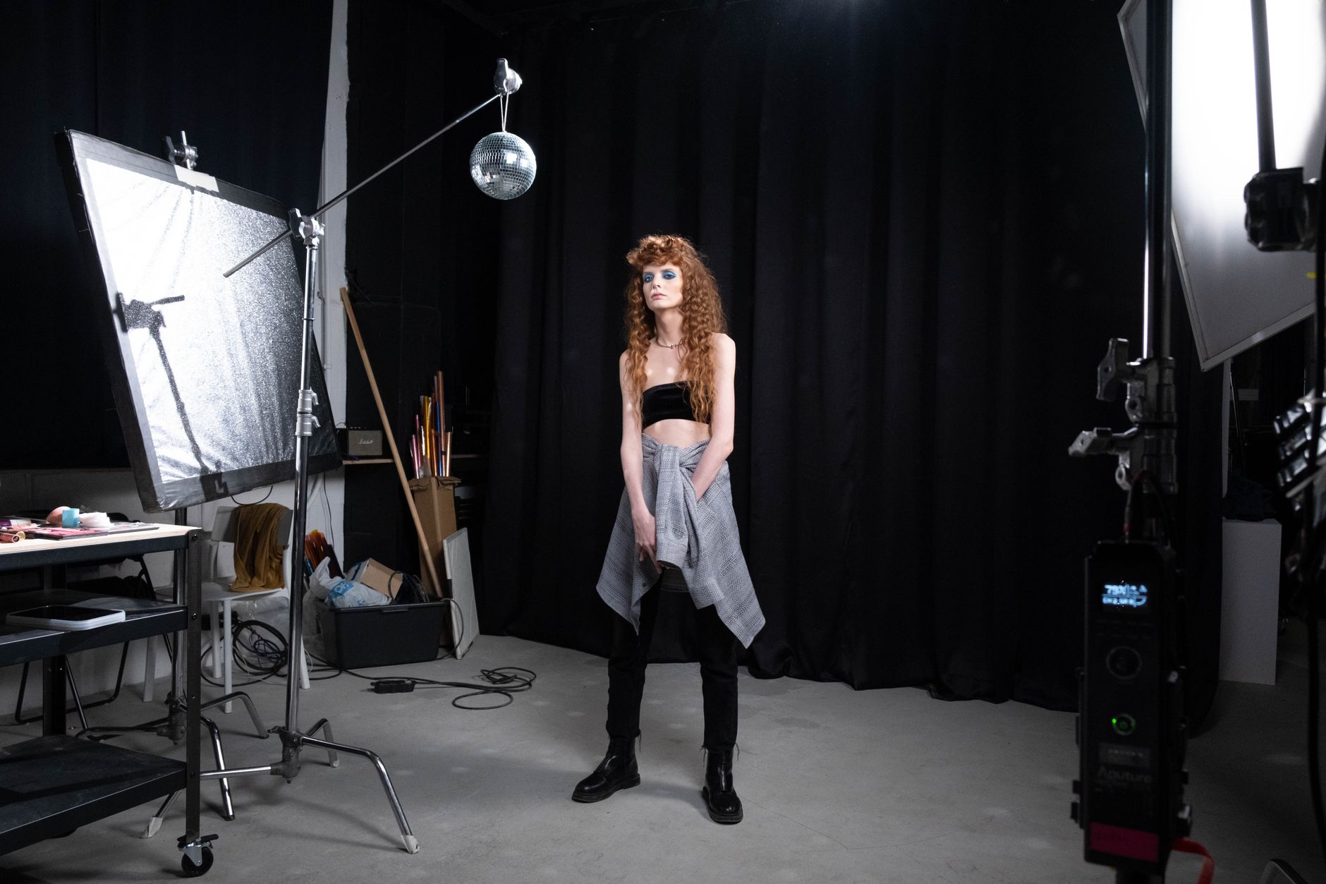 A stylish woman poses in a photo studio with professional lighting and props.