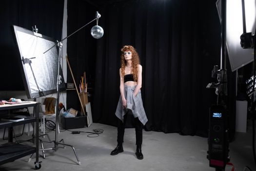 A stylish woman poses in a photo studio with professional lighting and props.