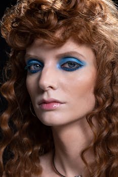 Close-up portrait of a young woman with striking blue eyeshadow and curly hair.