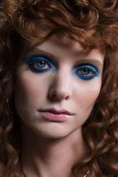 A striking close-up portrait of a redhead woman wearing bold blue eyeshadow, showcasing a unique makeup style.