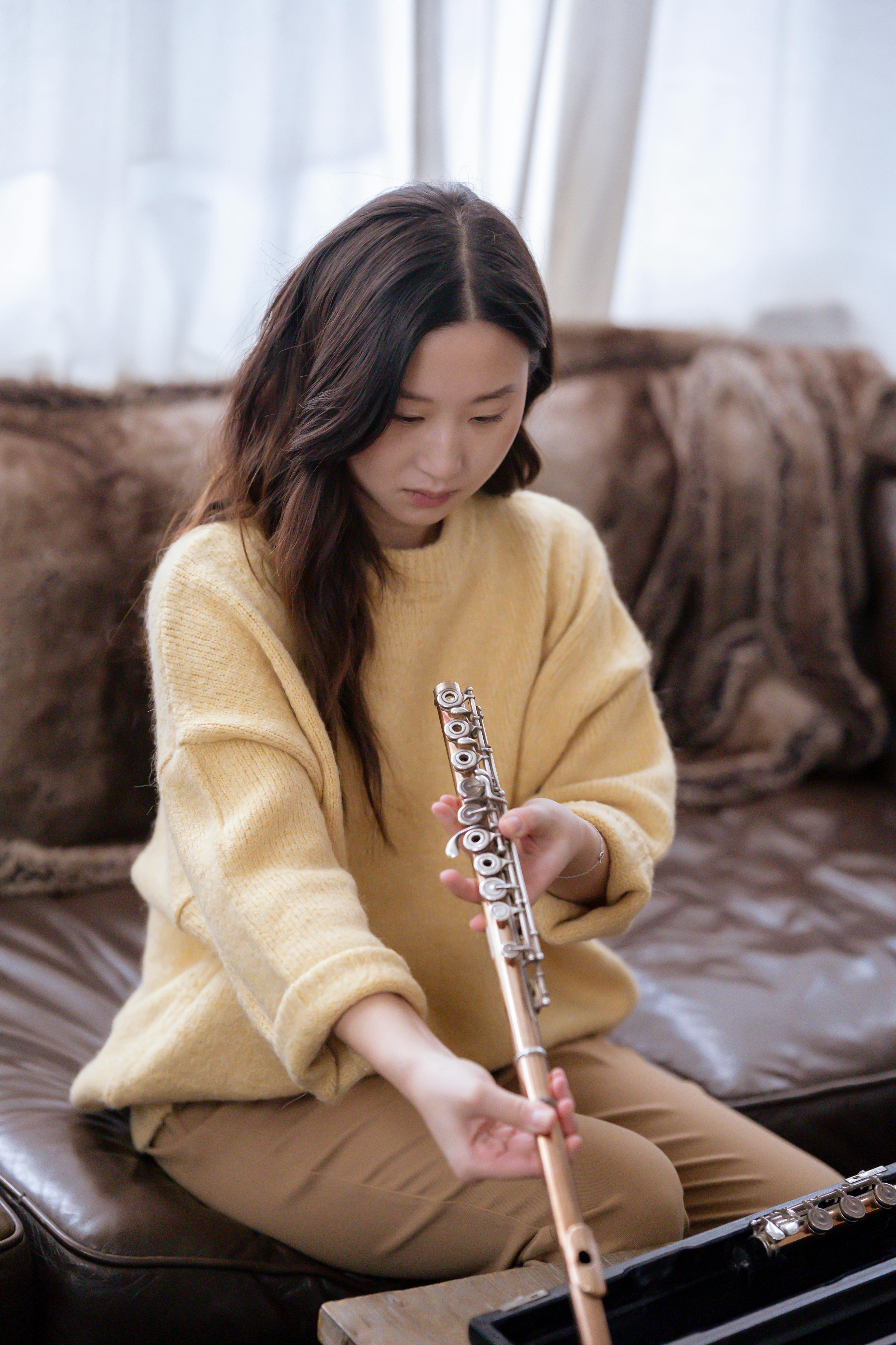asian lady examining flute on couch in room near table