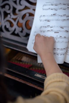 A hand turning a sheet music page on a classic piano, ideal for music education themes.