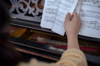 Unrecognizable woman turning page of music book near piano