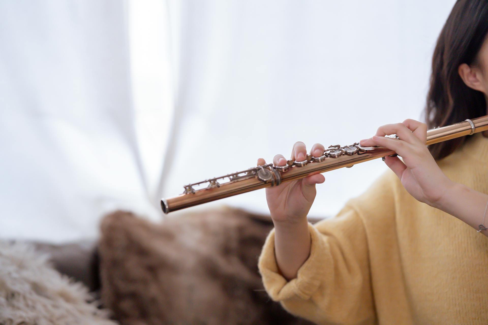 A woman practices flute playing indoors, capturing a serene musical moment.