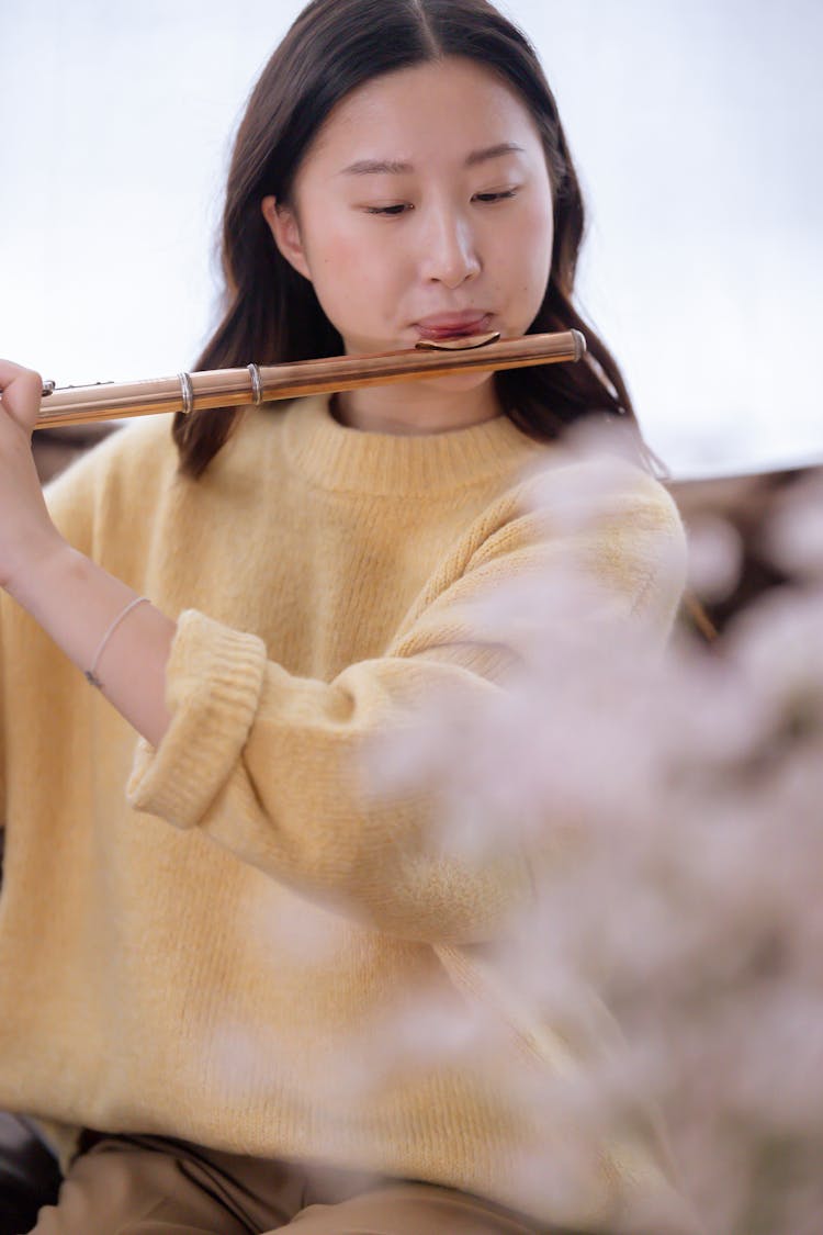 Asian Woman In Yellow Sweater Playing Flute