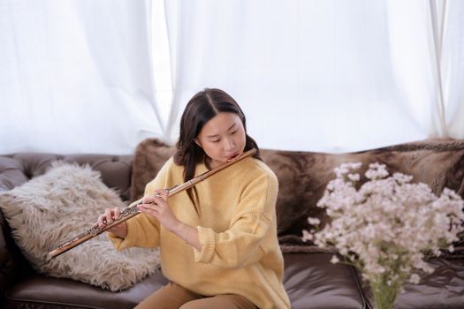 Asian female sitting on sofa and playing flute