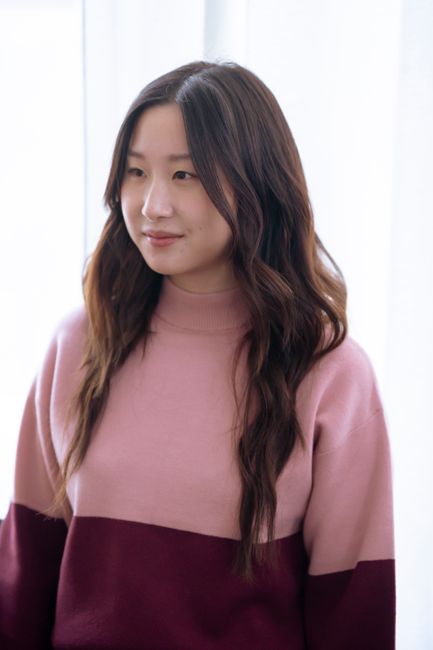 Confident young ethnic female wearing warm pink sweater while looking away in bright room