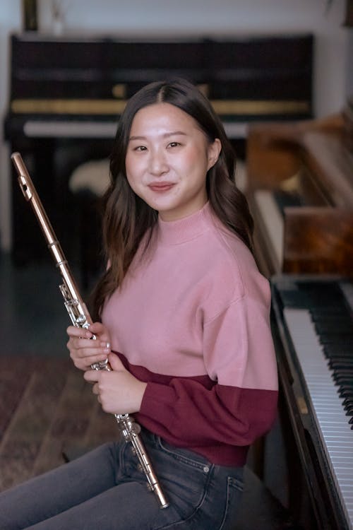 Asian woman sitting among pianos with flute in hands