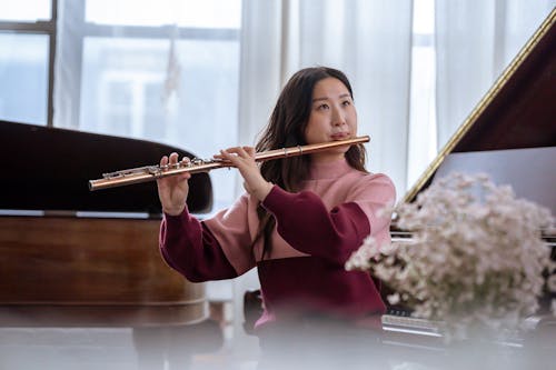 Asian lady playing on flute near piano in classroom