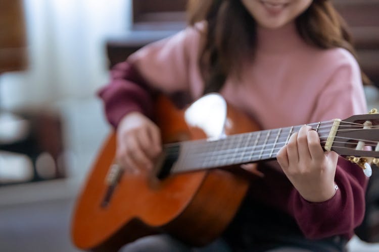 Crop Woman Playing Guitar Near Piano