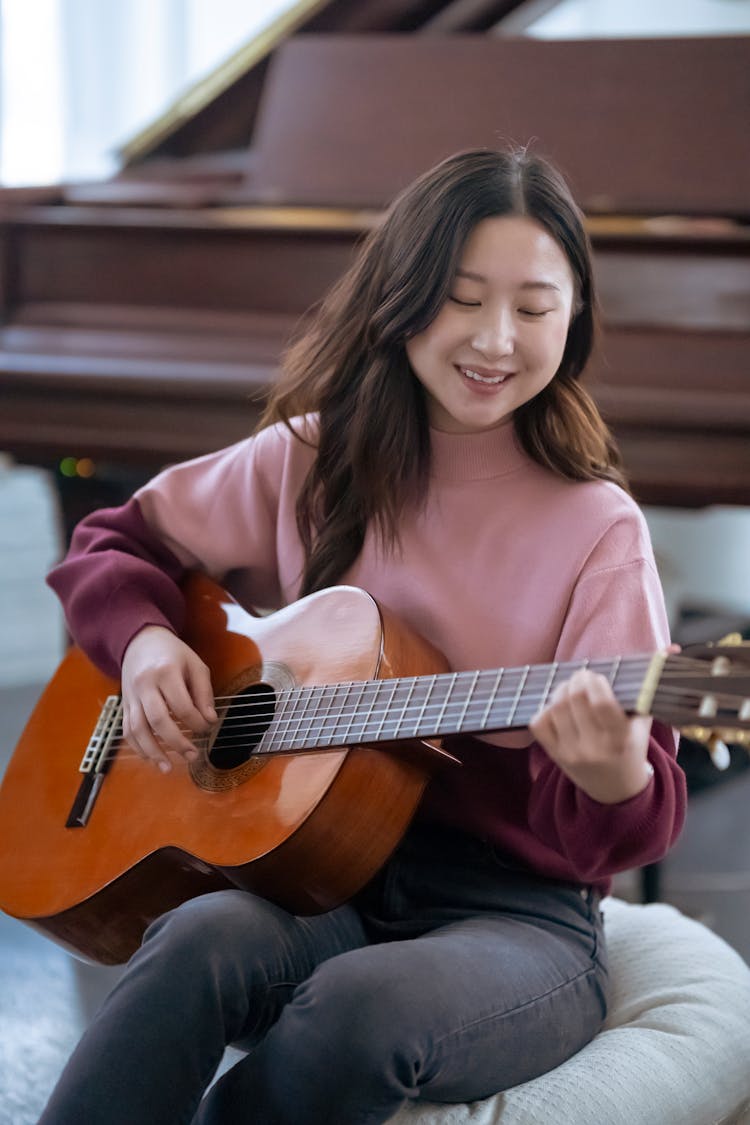 Positive Asian Woman Playing Guitar In Room