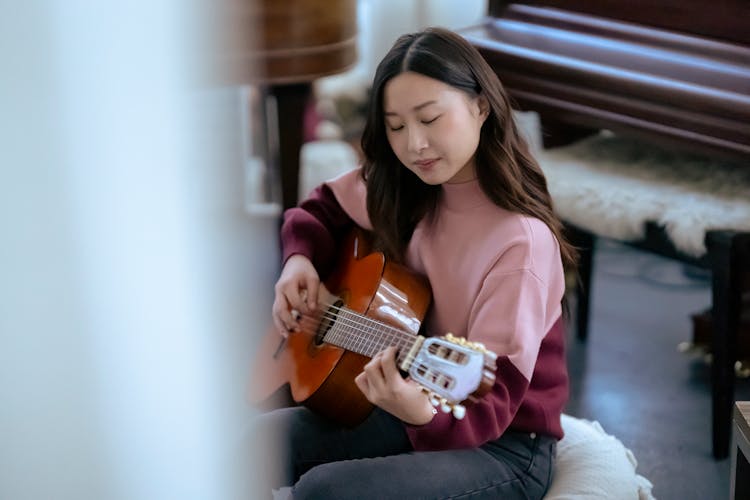 Focused Asian Woman Playing Guitar Near Piano