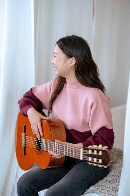 Smiling Asian woman with guitar on bed