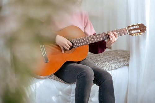 Crop woman playing guitar at bedroom with flowers