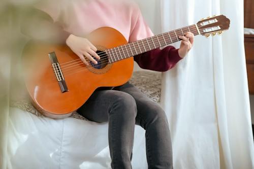 Unrecognizable musician performing song on guitar in bedroom
