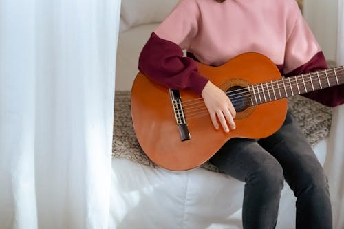 Crop woman playing guitar on bed