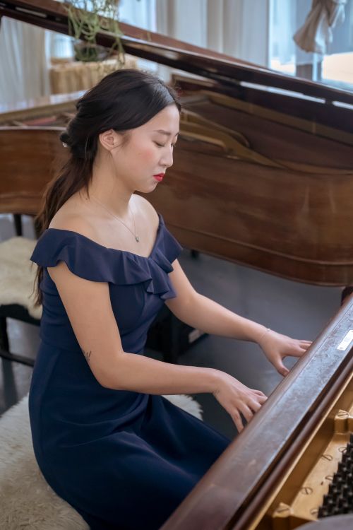 Free Side view of talented Asian female musician in elegant dress playing piano while rehearsing in light room during rehearsing at home Stock Photo
