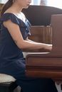 Side view of anonymous talented female with tattoo in stylish dress playing melody on piano while rehearsing in light room at home