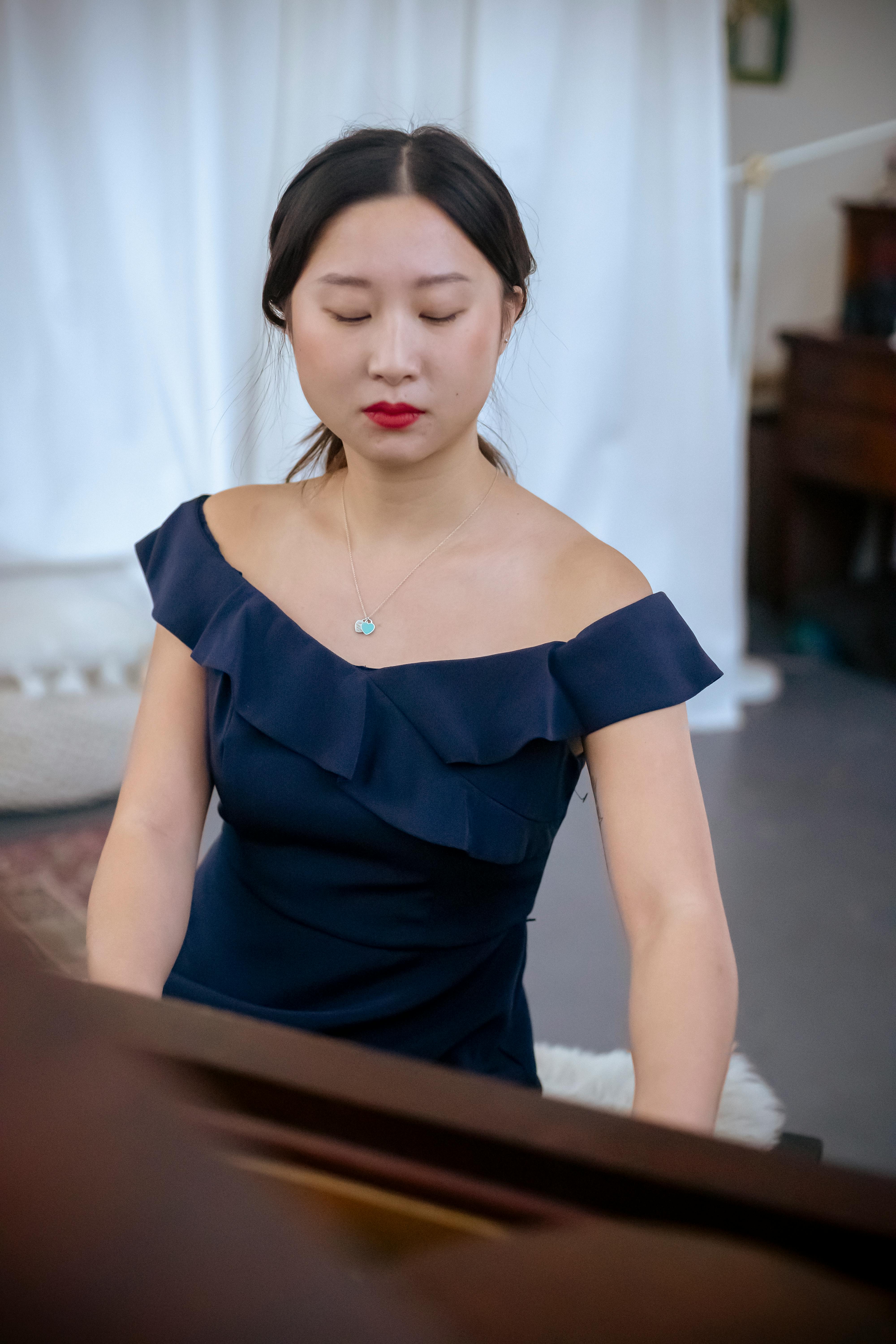 serious asian woman in posh dress playing piano