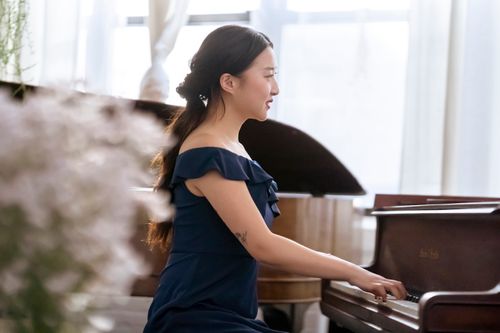 Free Side view of optimistic skilled Asian female musician playing piano while rehearsing in light room with window and blooming flowers Stock Photo