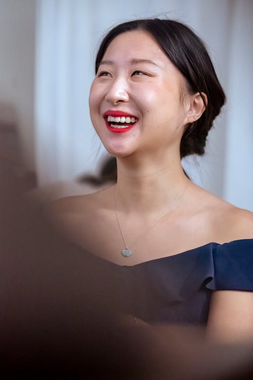 Low angle of ethnic female with precious pendant on chain wearing dress laughing happily and looking away