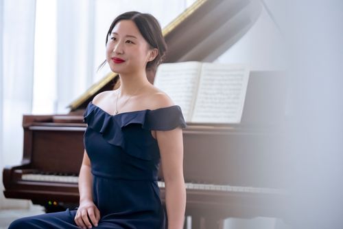 Free Smiling ethnic woman wearing elegant dress sitting near piano with music stand at concert and looking away Stock Photo