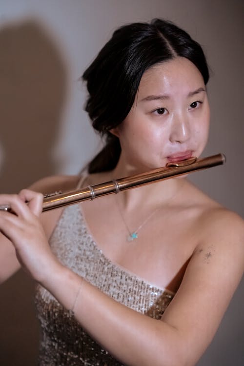 Ethnic female wearing dress playing flute at while at spotlight on stage at concert
