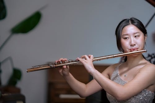 Talented ethnic female musician in shiny dress playing classic instrument flute while having live performance in concert hall