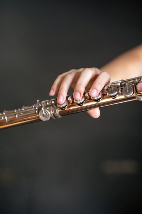 Unrecognizable professional talented player playing melody on long flute in light room on blurred background during rehearsal in creative studio