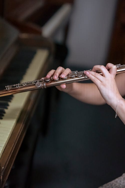 Crop woman playing flute near piano