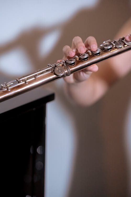 Faceless professional musician playing melody on long flute while standing near white wall during rehearsal in studio on blurred background