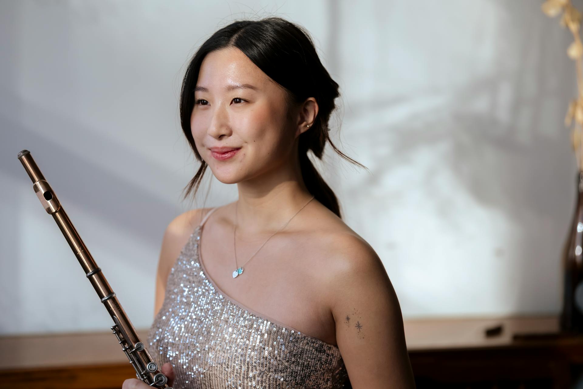 Talented ethnic female in elegant dress standing with flute in hands and happily smiling after successful performance